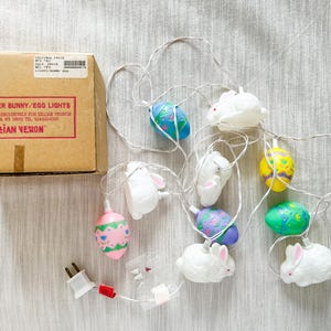 May include: Easter Bunny and egg lights with a cardboard box. The lights feature white bunny and colorful egg-shaped bulbs. The box reads "4674 Easter Bunny/Egg Lights" and "Lillian Vernon".