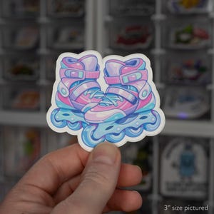 May include: A die-cut sticker featuring a pair of inline skates in shades of pastel pink, light blue, and purple. The skates have a boot design with straps, laces, and wheels, rendered in a cartoon style with a white border, labeled as 3 inches.