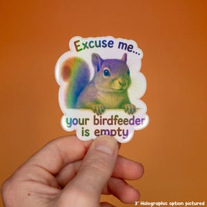May include: A holographic sticker featuring a squirrel with a rainbow-colored tail and fur. The text reads, Excuse me... your birdfeeder is empty. The sticker has a die-cut shape and a reflective finish that shifts colors under light, measuring 3 inches.