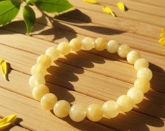 Puede incluir: Una pulsera elástica circular compuesta por cuentas redondas y lisas de color amarillo pálido. Las cuentas tienen un acabado pulido y semitranslúcido, ensartadas en un bucle continuo que crea una apariencia uniforme en toda la pieza.