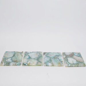 Puede incluir: Cuatro posavasos cuadrados hechos de rodajas pulidas de piedra &aacute;gata de color azul claro y blanco. Cada posavasos presenta un patr&oacute;n de mosaico &uacute;nico de segmentos minerales transl&uacute;cidos y opacos con vetas naturales y superficies lisas.