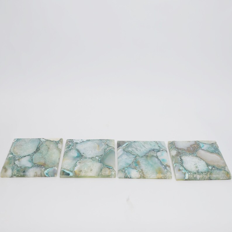 Puede incluir: Cuatro posavasos cuadrados hechos de rodajas pulidas de piedra &aacute;gata de color azul claro y blanco. Cada posavasos presenta un patr&oacute;n de mosaico &uacute;nico de segmentos minerales transl&uacute;cidos y opacos con vetas naturales y superficies lisas.