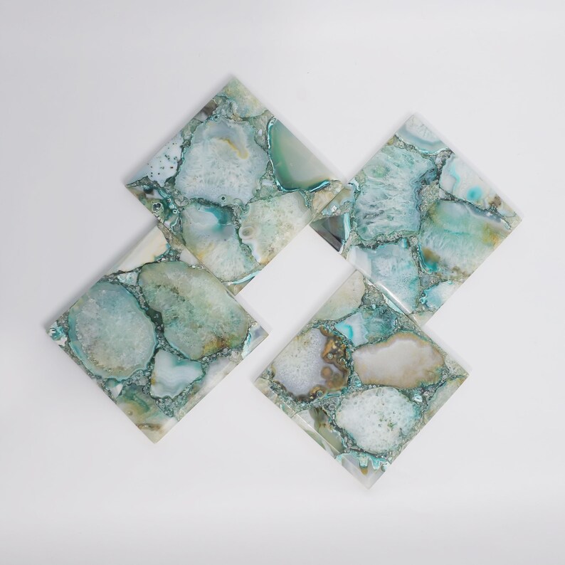 Puede incluir: Un juego de tres posavasos cuadrados hechos de rodajas de &aacute;gata pulida en tonos verde azulado, turquesa y blanco. Cada posavasos presenta una disposici&oacute;n tipo mosaico de fragmentos de piedra transl&uacute;cida con texturas cristalinas naturales y bordes lisos.