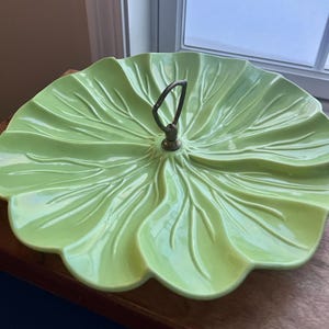May include: A light green ceramic serving platter with a leaf design. The platter has a scalloped edge and a metal handle for easy carrying. The serving dish is approximately 12 inches in diameter.