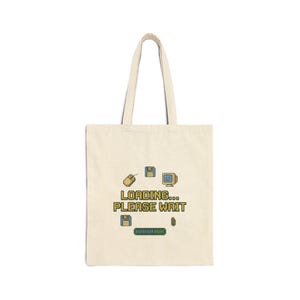 May include: A cream-colored tote bag with a retro computer graphic. The design includes a mouse, floppy disks, a computer monitor, and a loading bar, with the text "LOADING... PLEASE WAIT" in a pixelated font.