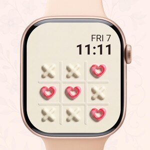 Op de afbeelding: Een roségouden smartwatch met een crèmekleurige wijzerplaat met een tic-tac-toe spel met harten en kruizen. De tijd is 11:11 uur en de dag is vrijdag. Het horloge heeft een lichtroze band.