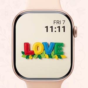 以下が含まれることがあります： クリーム色の文字盤のスマートウォッチには、カラフルで質感のある文字で「LOVE」という文字が表示されています。文字は赤、黄、青、緑で、下に緑と黄色の葉があります。時刻は金曜日の11時11分です。