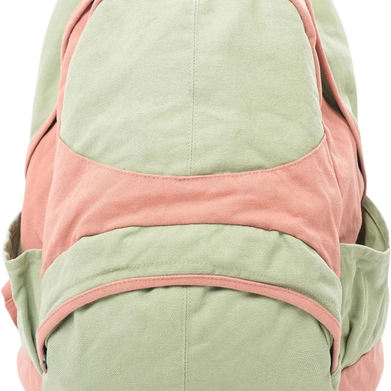 K&ouml;nnte beinhalten: Ein Rucksack aus Segeltuch mit einem Color-Block-Design in Salbeigr&uuml;n und ged&auml;mpftem Korallenrosa. Die Tasche verf&uuml;gt &uuml;ber ein gro&szlig;es Hauptfach, ein horizontales Vorderteil und zwei Seitentaschen, die alle mit sichtbaren N&auml;hten versehen sind.