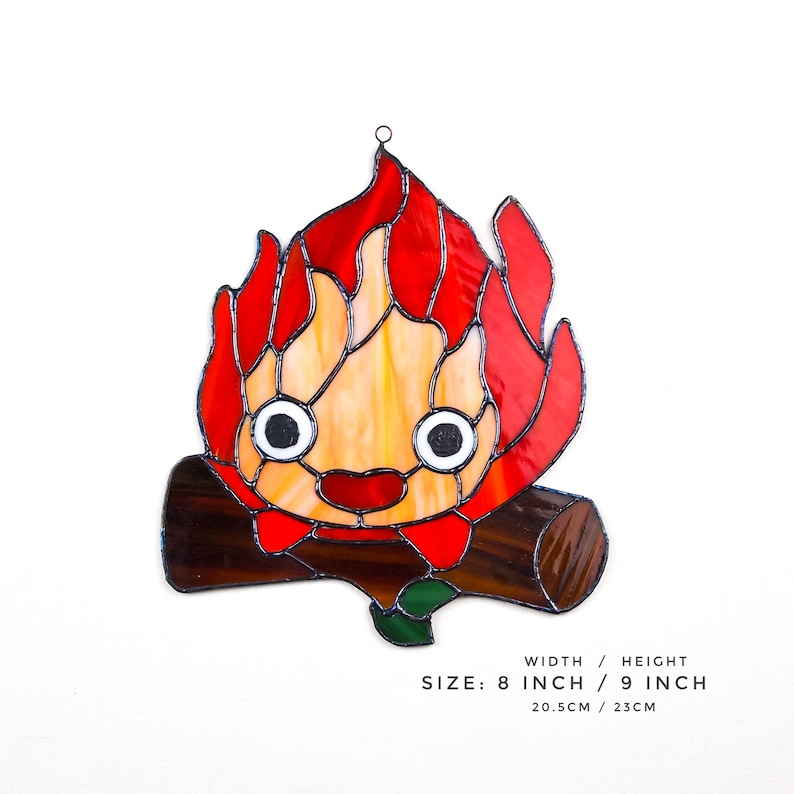 May include: Stained glass artwork depicting a cartoon flame character with a smiling face, set on a log. The flame is red, orange, and yellow. The artwork is 8 inches wide and 9 inches high.