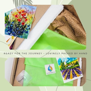 May include: An open cardboard box with art prints and packaging materials. The prints feature watercolor paintings of flowers and landscapes. The text "READY FOR THE JOURNEY - LOVINGLY PACKED BY HAND" is visible.