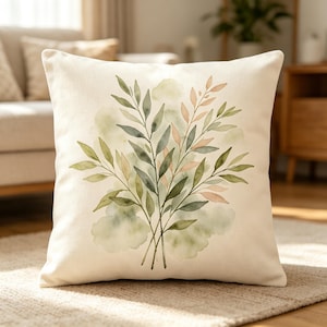 May include: Square cushion featuring a watercolour design of green and peach-coloured leaves and branches. The leaves are arranged in a bouquet against a soft green background on a cream-coloured cushion.