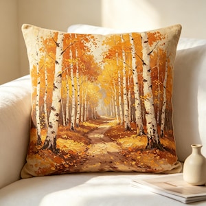 May include: A square throw pillow featuring a printed landscape scene of a birch forest during autumn. The design displays white-barked trees with vibrant orange and yellow foliage lining a dirt path covered in fallen leaves under soft light.