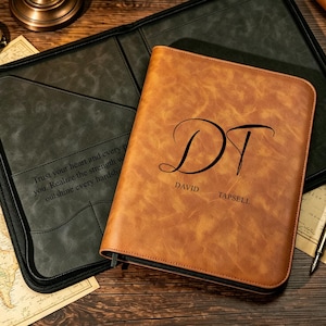 Op de afbeelding: Een beige lederen portfolio met het monogram DT en de naam David Tapsell gegraveerd op de voorkant. De binnenkant is bekleed met donkergrijs materiaal en bevat de tekst Trust your heart and every path you. Realize the strength within to outshine every hardship.
