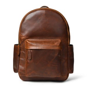 May include: A brown leather backpack with a rounded top and a front pocket. The backpack has two side pockets and a top handle. The leather has a distressed look, with variations in color and texture. The zipper pulls are visible.