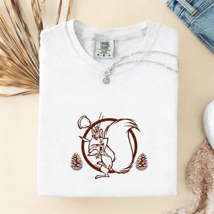 May include: White t-shirt with a brown cartoon squirrel graphic, a silver necklace, and the text "Ongoing Exodus" on the tag. The squirrel is inside a brown circle with two brown pinecones on either side.