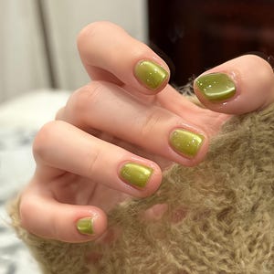 May include: Short, square-shaped fingernails featuring a glossy, metallic olive green cat-eye polish finish. The nail color displays a shimmering, reflective light-catching streak across the center of each nail, creating a dimensional effect.