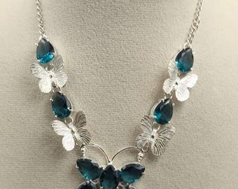 May include: Silver-toned necklace featuring a butterfly design. The necklace has a chain and is adorned with teal-colored teardrop-shaped gemstones and silver butterfly accents. The central butterfly design is composed of multiple gemstones.