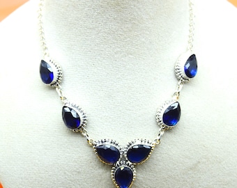 May include: A silver necklace featuring teardrop-shaped, deep blue gemstones. The gemstones are set in ornate, textured silver settings and connected by a delicate chain. The necklace is displayed on a neutral background.