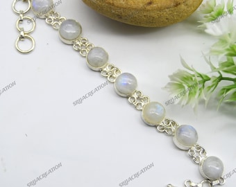 May include: A silver bracelet featuring seven round, iridescent moonstone cabochons. The stones are set in ornate, openwork silver settings. The bracelet has a toggle clasp and is displayed on a white surface.