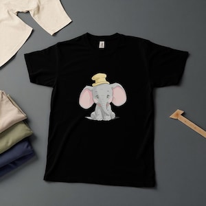 May include: Black t-shirt featuring a cartoon elephant with large pink ears and a yellow hat. The elephant is sitting and has a gray body. The t-shirt is made of a soft material and is suitable for casual wear.