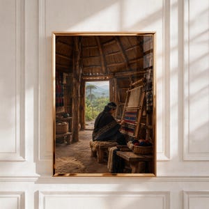May include: A framed wall art print depicting a person in a dark shawl sitting on a wooden bench inside a rustic thatched-roof structure, weaving a colorful patterned textile on a wooden loom, with a view of a green landscape through the doorway.