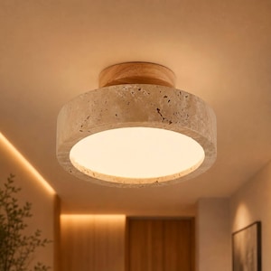 Könnte beinhalten: Eine moderne Deckenleuchte mit einem kreisförmigen Schirm in Betonoptik und einem Holzsockel. Das Licht strahlt ein weiches, warmes Leuchten aus. Die Leuchte ist für die bündige Montage konzipiert und sorgt für Umgebungslicht. Das Design ist minimalistisch und für verschiedene Einrichtungsstile geeignet.