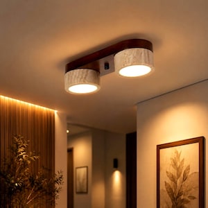 Puede incluir: Una lámpara de techo empotrada con una base de madera marrón oscuro y dos pantallas cilíndricas con un acabado de piedra texturizada de color claro. La lámpara emite un brillo cálido y suave desde ambas fuentes de luz circulares.