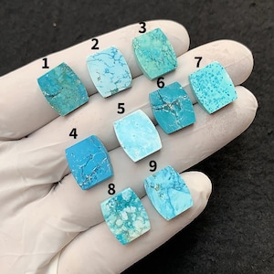 Puede incluir: Nueve cabujones de piedras preciosas turquesas en varios tonos de azul y verde, cada uno con patrones de vetas únicos. Las piedras son rectangulares con esquinas redondeadas, exhibidas sobre una superficie blanca.