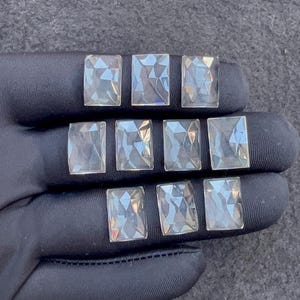 Puede incluir: Diez gemas rectangulares transparentes con superficies facetadas. Las gemas están dispuestas sobre una superficie negra, mostrando su claridad y corte. Es probable que estas gemas sean para la fabricación de joyas o manualidades.