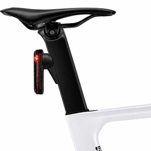 Könnte beinhalten: Ein schwarzer Fahrradsattel auf einer schwarzen Sattelstütze mit schlankem Profil und einem roten LED-Sicherheitslicht an der Rückseite. Die Sattelstütze ist mit einem weißen Fahrradrahmen verbunden, was ein schlankes Design zeigt.