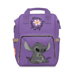 Könnte beinhalten: Ein lila Rucksack mit einem Cartoon-Bild von Stitch, der eine Schildkröte hält. Der Rucksack hat einen oberen Griff, Seitentaschen und eine Vordertasche. Der Text "Ohana Means Family" ist oben aufgedruckt.