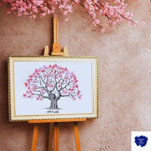 Può includere: Una stampa artistica incorniciata di un albero con bordo dorato, esposta su un cavalletto di legno. L'albero presenta un tronco e rami con foglie di impronte digitali rosa e viola. Un cuore è disegnato sul tronco. Fiori rosa sullo sfondo.