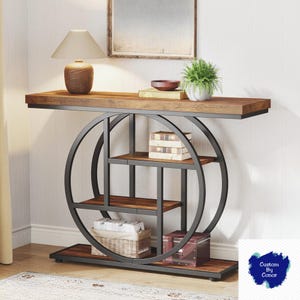 May include: A modern console table with a dark wood top and shelves. The table features a black metal frame with a circular design and multiple shelves for storage. A lamp, books, and decorative items are displayed on the table's surface. The table measures approximately 60 inches long.