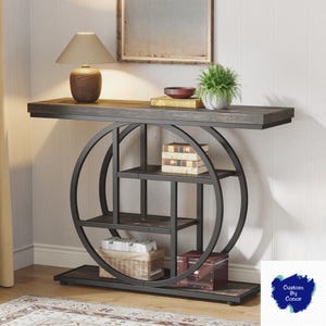 Peut inclure: Une console en bois fonc&eacute; avec un plateau gris et une structure en m&eacute;tal noir. La table a un design circulaire avec des &eacute;tag&egrave;res et est d&eacute;cor&eacute;e d'une lampe, de livres et d'une plante. La table mesure 152 cm de long, 41 cm de large et 76 cm de haut.