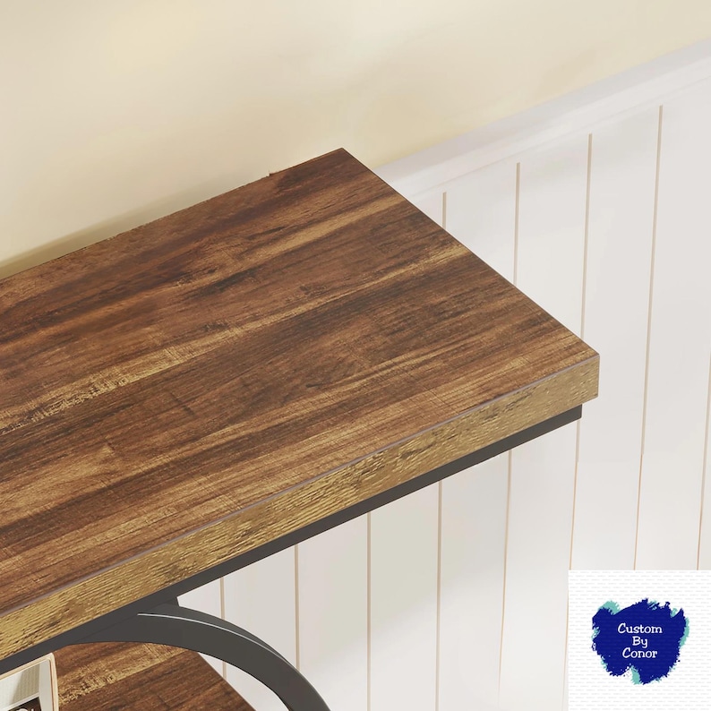 Peut inclure: Gros plan sur une table en bois avec une finition marron fonc&eacute;. La table a un cadre en m&eacute;tal noir et est plac&eacute;e contre un mur &agrave; panneaux blancs. La surface de la table pr&eacute;sente un motif de grain de bois.