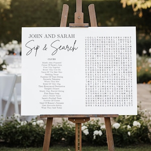 May include: A white rectangular wedding sign on a wooden easel featuring the text John and Sarah Sip & Search. The sign includes a list of clues and a word search puzzle grid with various letters. The design uses black serif and script fonts.