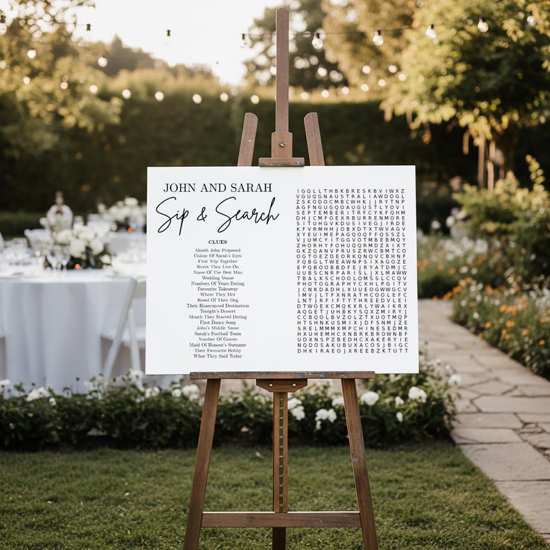 May include: A white rectangular wedding sign on a wooden easel featuring the text John and Sarah Sip & Search. The sign includes a list of clues and a word search puzzle grid with various letters. The design uses black serif and script fonts.