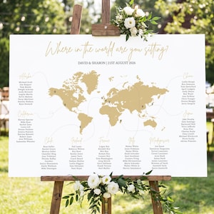 以下が含まれることがあります： 金色の世界地図、"Where in the world are you sitting?"、"DAVID & SHARON | 21ST AUGUST 2026"という文字、および地理的な場所ごとに整理された名前のリストが記載された白い結婚式の座席表ボード。木製のイーゼルに立てかけられています。