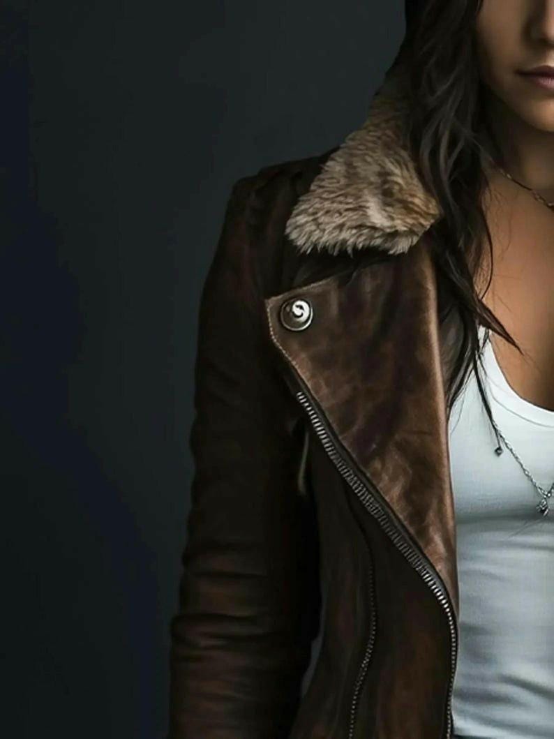 Puede incluir: Chaqueta de cuero marr&oacute;n con cuello de piel sint&eacute;tica y cremallera plateada. La chaqueta tiene un detalle de bot&oacute;n en el hombro y se usa sobre una camiseta sin mangas blanca. La est&eacute;tica general es casual y elegante.