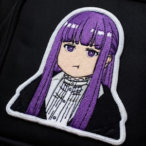 May include: Embroidered patch featuring an anime-style character with long purple hair and purple eyes. The character wears a black jacket over a white collared shirt. The patch has a white border and is affixed to a black backpack.