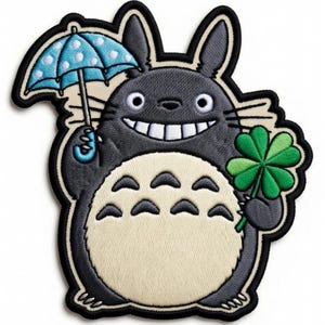Puede incluir: Parche bordado que representa un personaje de dibujos animados gris que sostiene un paraguas azul con lunares y un trébol verde de cuatro hojas. El personaje tiene una gran sonrisa y una barriga color crema. El parche tiene un borde negro.