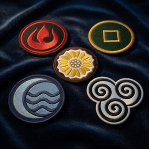 May include: Five embroidered patches with symbols from a fantasy series. The patches include a flame, a square within a circle, a flower, a moon and waves, and a swirling air symbol. The patches are in various colours, including red, green, blue, and white.
