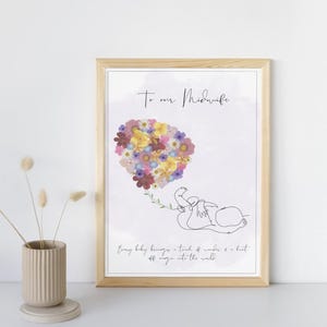 May include: A framed print with a light wood frame. The artwork features a line drawing of a baby and a heart-shaped arrangement of colorful flowers. The text "To our Midwife" and a quote are also included.