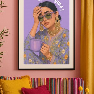 May include: Art print of a woman in a purple floral outfit, wearing sunglasses and gold jewelry, holding a purple mug. The artwork has the text "SIRR NA KHAA!" above the woman's head. The print is framed in a black frame.