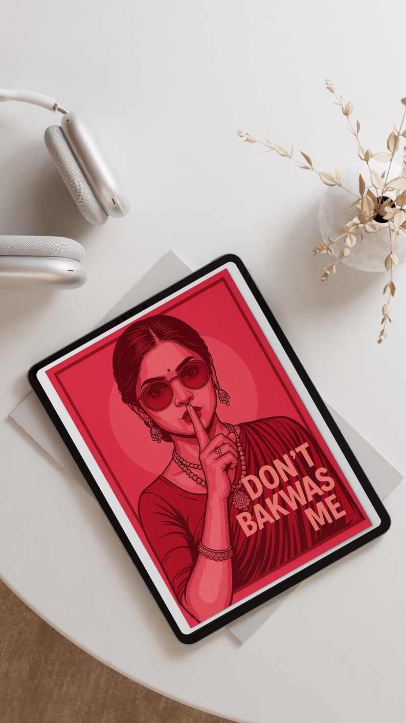 May include: Red and black tablet with a graphic of a woman wearing sunglasses and jewelry, with the text "DON'T BAKWAS ME". The tablet is on a white surface, with white headphones and a vase of dried flowers in the background.