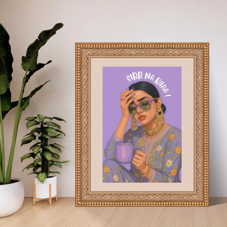 May include: Framed art print featuring a woman with sunglasses, holding a purple mug, and wearing a floral patterned outfit. The text "SIRR NA KHAA!" is displayed above the woman's head. The frame is gold.
