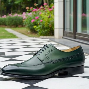 May include: A single, dark green leather dress shoe with black laces and a black sole. The shoe features decorative perforations and a cap toe. The shoe is set on a black and white checkered surface.