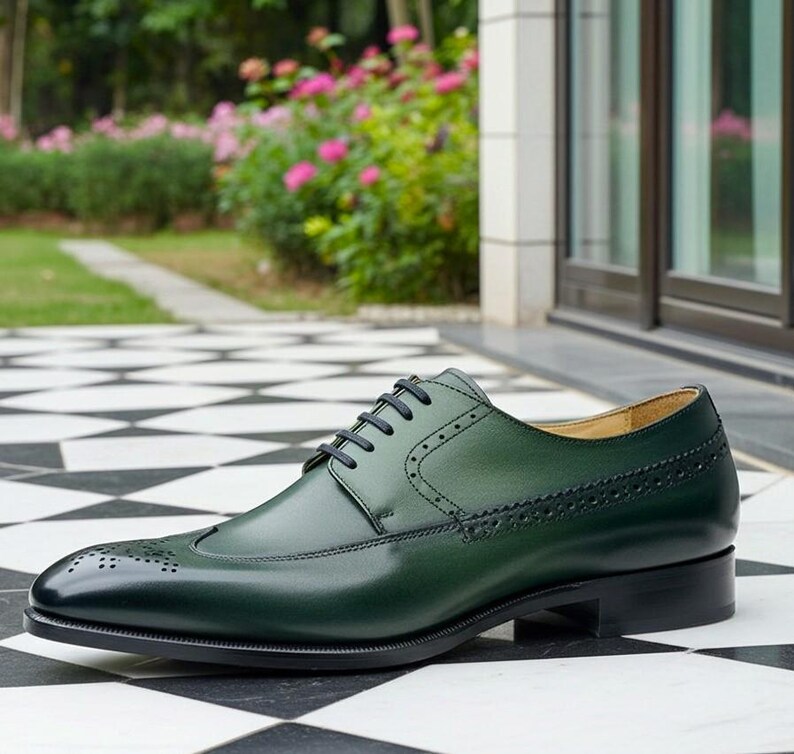 May include: A single, dark green leather dress shoe with black laces and a black sole. The shoe features decorative perforations and a cap toe. The shoe is set on a black and white checkered surface.