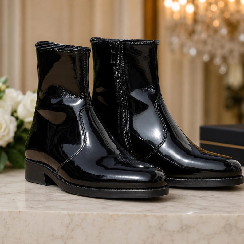 May include: A pair of black ankle boots with a high-gloss patent finish. These boots feature a sleek, rounded toe, a low block heel, and a vertical zipper closure on the inner side of each boot, extending from the sole to the top of the shaft.