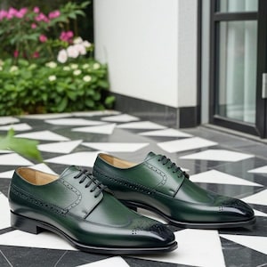 May include: A pair of green leather dress shoes with black laces and black toe caps. The shoes have decorative perforations and are displayed on a black and white tiled surface. The shoes are a classic style.